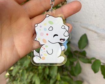 May include: A white, cartoon-style dinosaur keychain with colorful polka dots. The dinosaur is smiling and has a light blue outline.