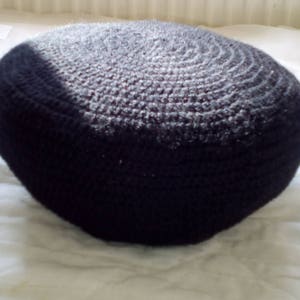 May include: A black crocheted round cushion with a textured surface.