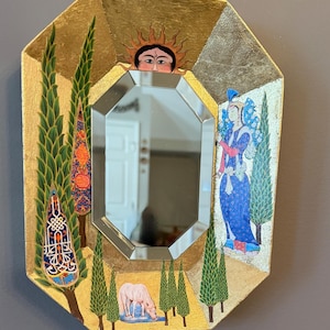 May include: An octagonal decorative mirror with a gold-colored frame. The frame features painted illustrations of trees, a figure in blue, and a sun. The mirror's center is a multi-faceted shape, reflecting the room. A pink horse drinks from a pond.