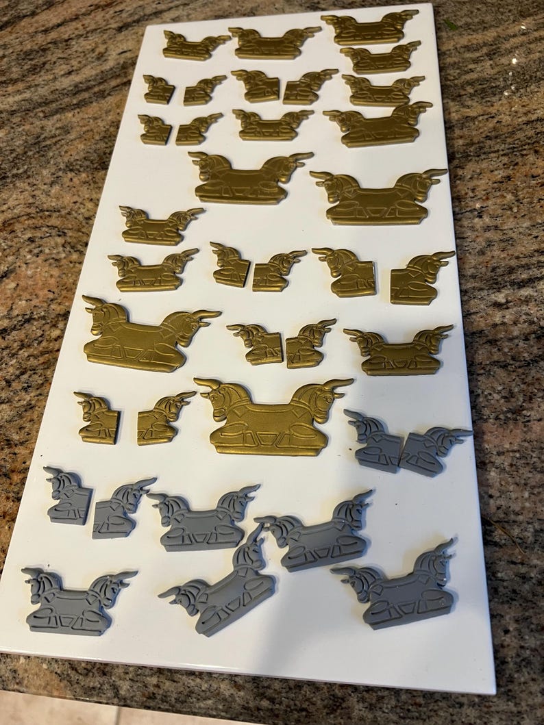 May include: A collection of gold and gray decorative horse-shaped embellishments arranged on a white surface. The embellishments vary in size and are likely for crafting or decorative purposes. The horses are in various poses.
