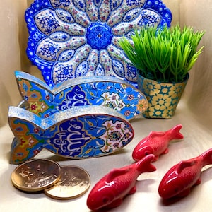 May include: A decorative arrangement featuring a large blue and white patterned plate, two fish-shaped holders with intricate designs, and three small red fish figurines. A small potted plant and two coins are also present.
