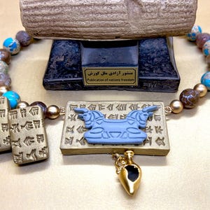 May include: A necklace with a pendant featuring a blue bull design and a small gold-colored amphora. The necklace has a beaded strand with blue, brown, and gold beads. Two rectangular pendants with ancient writing are also included.