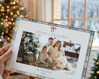 May include: A Christmas card with a family photo, plaid border, and the words "MERRY CHRISTMAS." The card is held in front of a decorated Christmas tree and a fireplace. The card also includes the family name and the year 2023.