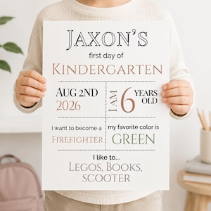 May include: A white rectangular sign with black and muted red text reading Jaxon's first day of Kindergarten, Aug 2nd 2026, I am 6 years old, I want to become a firefighter, my favorite color is green, and I like to Legos, books, scooter.