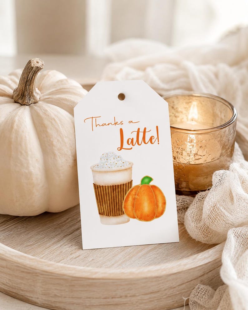 May include: A white pumpkin and a tag with the words "Thanks a Latte!" and a watercolor illustration of a latte and a pumpkin. A lit candle in a glass holder is also visible.