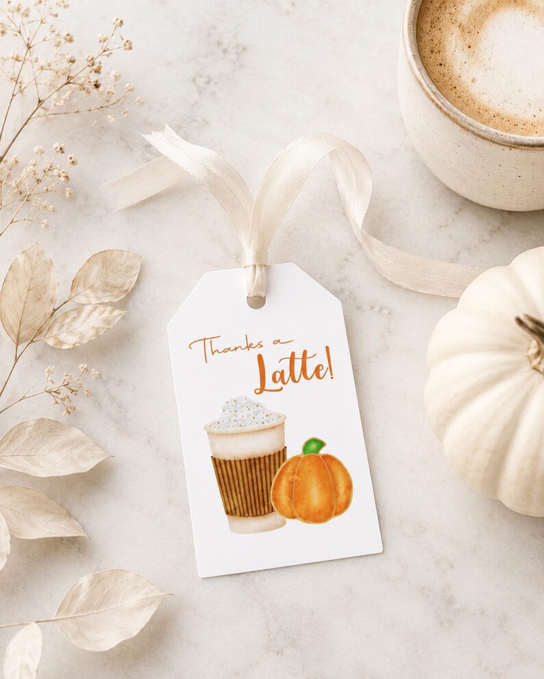 May include: A white gift tag with the text "Thanks a Latte!" features a watercolor illustration of a coffee cup and a pumpkin. A beige ribbon is attached to the tag. A cup of coffee and a white pumpkin are also in the image.