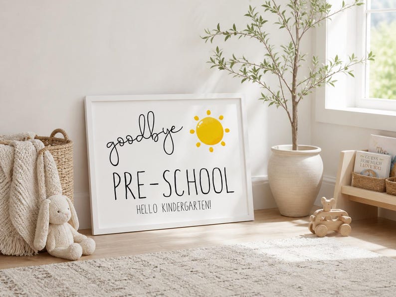 Puede incluir: Un letrero blanco enmarcado con las palabras "goodbye PRE-SCHOOL" y "HELLO KINDERGARTEN" en escritura negra. Un sol amarillo est&aacute; a la derecha de "goodbye". El letrero est&aacute; sobre una alfombra clara.