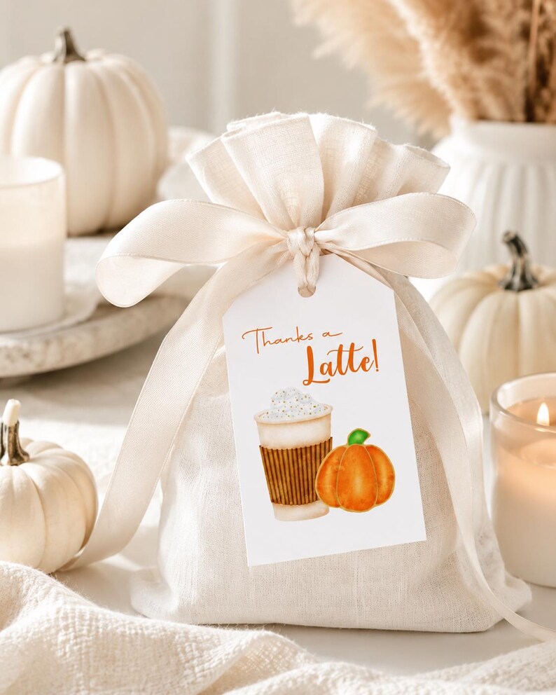 May include: A beige fabric gift bag tied with a cream ribbon, with a tag that reads "Thanks a Latte!" and features a watercolor illustration of a latte and a pumpkin. White pumpkins and candles are in the background.