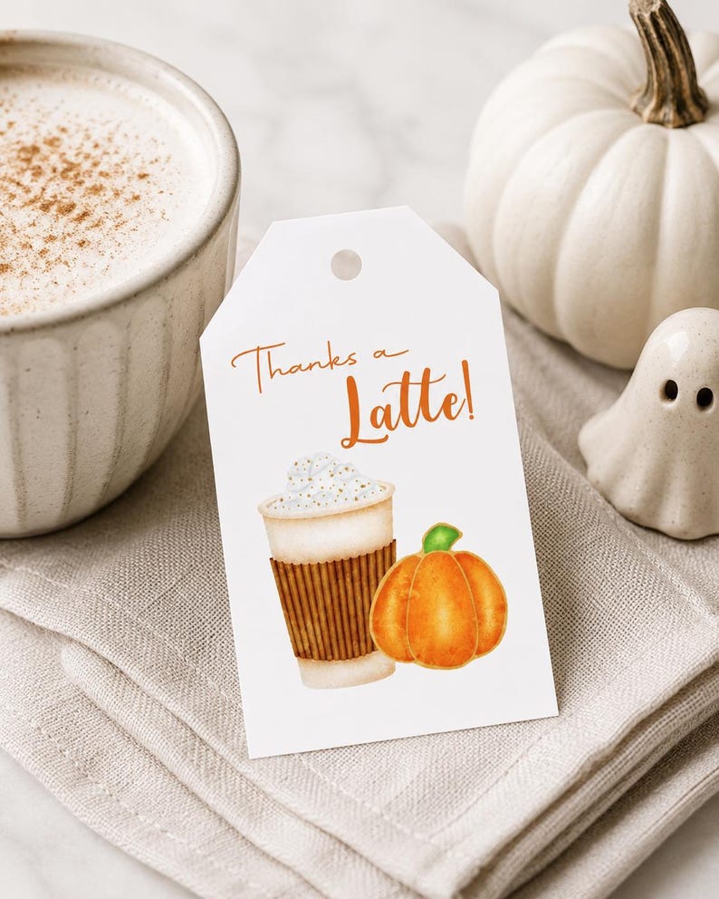 May include: A white gift tag with the text "Thanks a Latte!" in orange script. The tag features a watercolor illustration of a latte and a pumpkin. A cup of coffee and a white pumpkin are in the background.