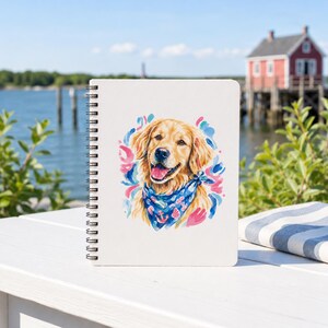 May include: Spiral-bound notebook featuring a watercolor illustration of a Golden Retriever. The dog wears a blue bandana with anchor designs and is surrounded by pink and blue brushstrokes. The notebook is on a white surface.