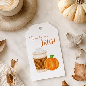 May include: A white gift tag with the text "Thanks a Latte!" features a watercolor illustration of a coffee cup and a pumpkin. A cup of coffee and a small pumpkin are also visible.