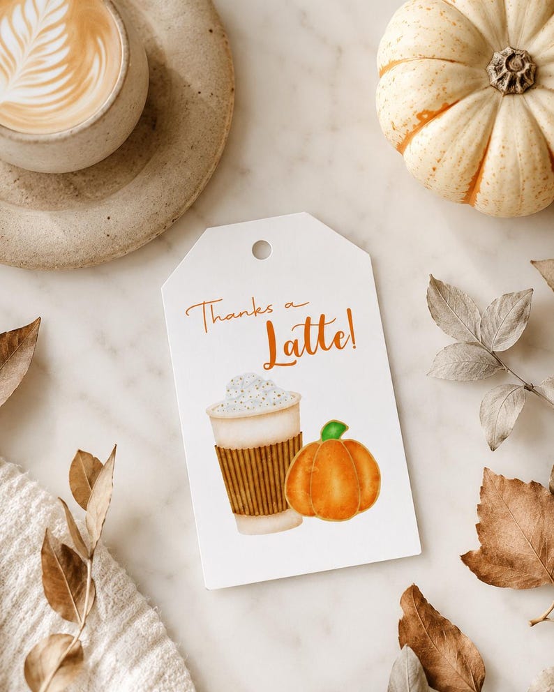May include: A white gift tag with the text "Thanks a Latte!" features a watercolor illustration of a coffee cup and a pumpkin. A cup of coffee and a small pumpkin are also visible.