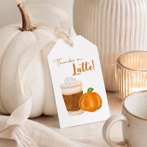 May include: A white tag with the text "Thanks a Latte!" features a watercolor illustration of a latte and a pumpkin. A white pumpkin and a ceramic mug are in the background, suggesting a fall or autumn theme.