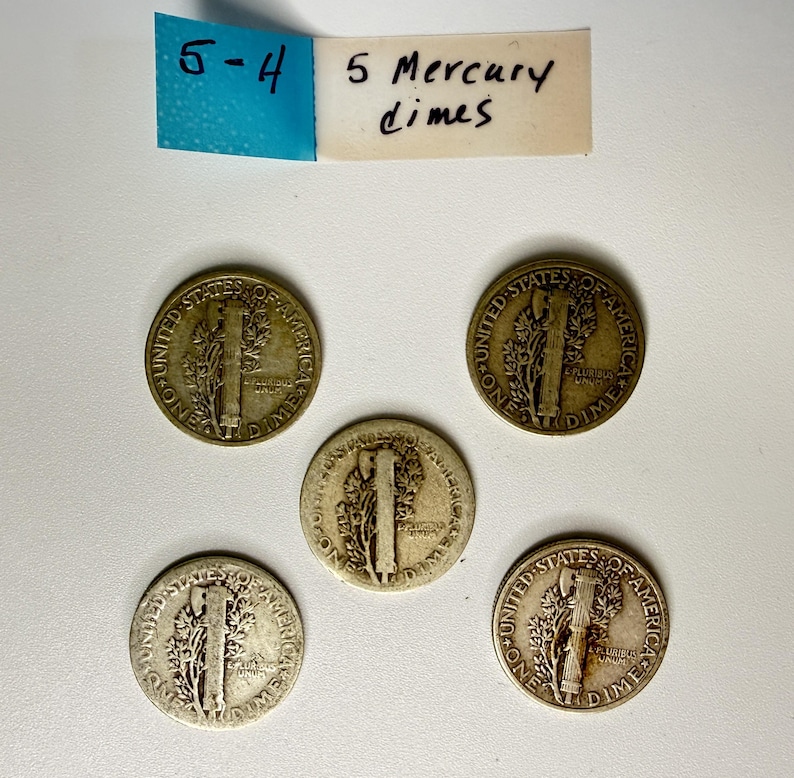May include: Five silver-colored United States Mercury dimes arranged in a cluster. Each coin displays the reverse side featuring a fasces and olive branch. Above the coins, a white paper label with blue tape reads 5-4 and 5 Mercury dimes.