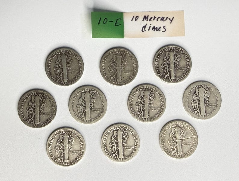 May include: Ten silver-colored United States Mercury dimes arranged in a group. Each coin features the reverse side showing a fasces and an olive branch with the text United States of America and One Dime. A paper label reads 10-E 10 Mercury dimes.