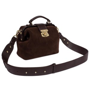 May include: A brown leather doctor's bag with a gold lock and a long adjustable strap. The bag is made of suede and has a vintage look.