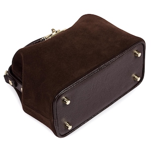 May include: A brown suede and leather handbag with a gold clasp and four gold feet.