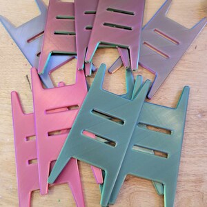 May include: A pile of iridescent plastic stands in pink, teal, and silver. The stands are shaped like a ladder with three rungs and have a flat base.