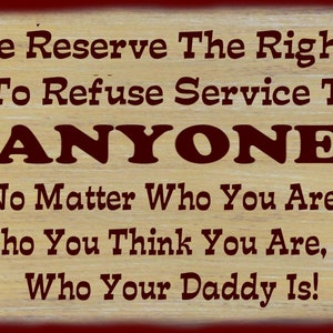 May include: A wooden sign with a red border and brown wood grain background. The sign reads "We Reserve The Right To Refuse Service To ANYONE No Matter Who You Are, Who You Think You Are, Or Who Your Daddy Is!"
