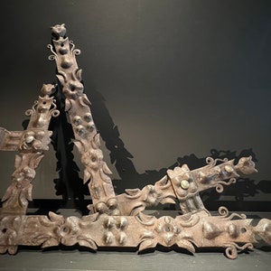 Könnte beinhalten: Drei verzierte Metallwinkel mit aufwendigen floralen Designs. Die Winkel sind aus dunklem Metall gefertigt und haben ein rustikales Aussehen.