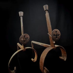Peut inclure: Une paire de chenets de cheminée antiques avec un motif de croix décoratif. Les chenets sont en métal et ont une finition rustique et vieillie.