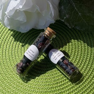 May include: Two small glass bottles filled with dark red garnet crystals. The bottles have cork stoppers and labels that read "Garnet Inspires Love Root Chakra".