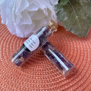 May include: Two small glass bottles filled with amethyst crystals. The bottles have cork stoppers and labels that read "Amethyst, Bring Peace, Crown Chakra".