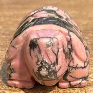 May include: A pink and black carved stone turtle figurine. The turtle is made of a pink and black stone with a marbled pattern.