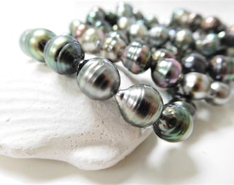 May include: A strand of black Tahitian pearls with iridescent green and blue hues. The pearls are round and smooth, and they are strung on a white cord.