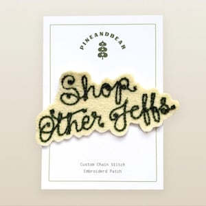 Puede incluir: Un parche de fieltro color crema con bordado en punto de cadeneta verde oscuro que dice Shop Other Jeffs. El parche está montado sobre una tarjeta de presentación blanca con el texto Pineandbear y Custom Chain Stitch Embroiderd Patch.