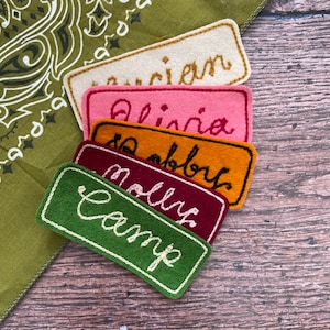May include: Five felt name tags with white stitching. The names are "Camp", "Molly", "Bobby", "Olivia", and "Lauren".