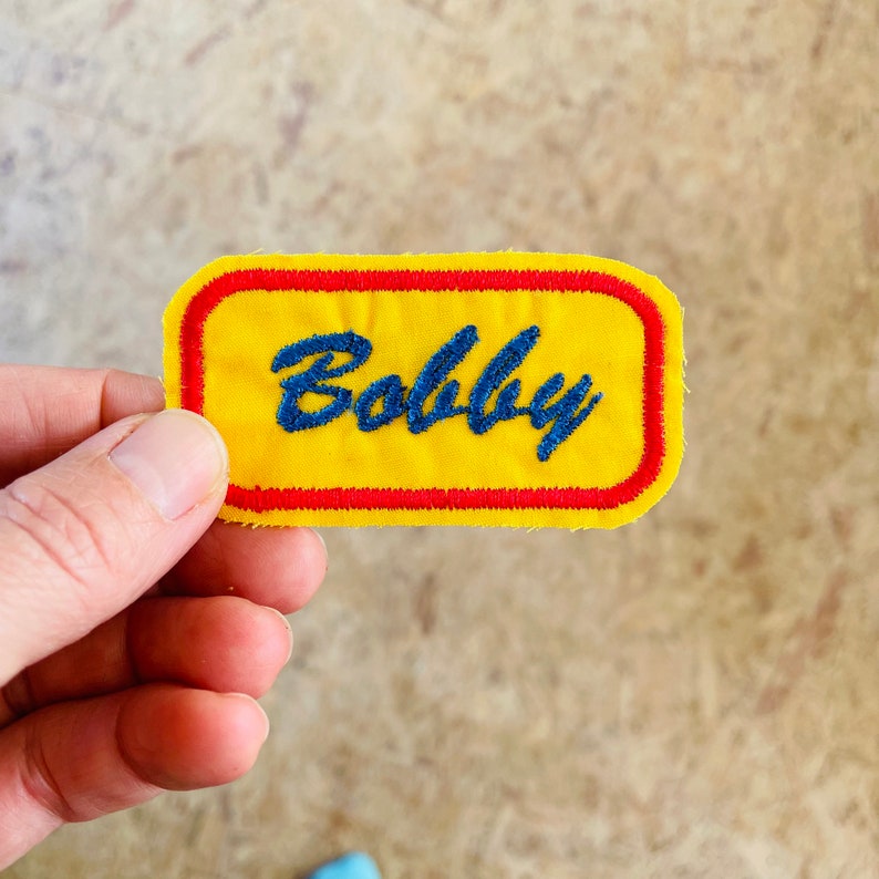Retro embroidered name patch in yellow and red.