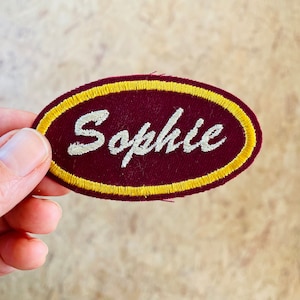 Retro embroidered name patch in burgundy and yellow.