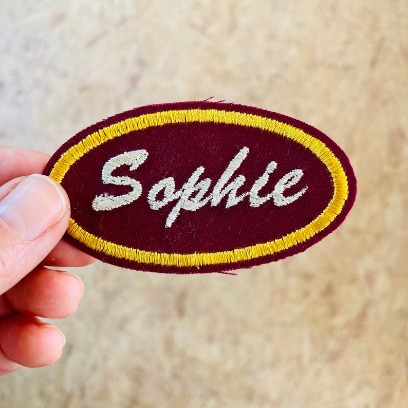 Retro embroidered name patch in burgundy and yellow.