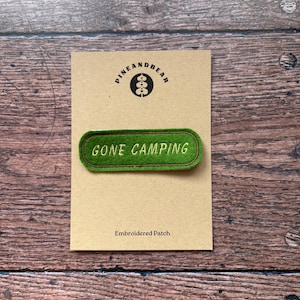 May include: A green embroidered patch with the text "GONE CAMPING" in white, set against a tan background. The patch is rectangular with rounded corners and a dark green border. The card also features a logo and the words "Embroidered Patch".