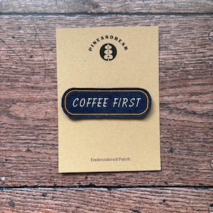 May include: Embroidered patch with the text "COFFEE FIRST" in white, set against a navy blue background with a gold border. The patch is on a tan card with the "PINEANDBEAR" logo and the words "Embroidered Patch".