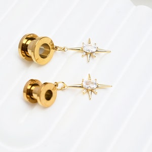 May include: Two gold star-shaped earrings with clear crystal accents. The earrings are attached to gold metal plugs.