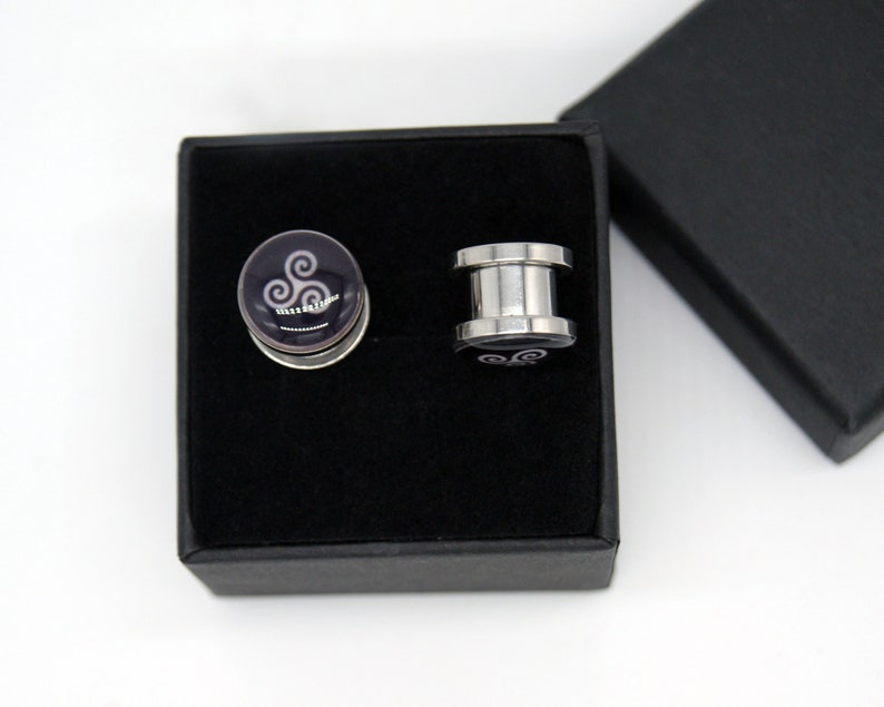 May include: A pair of silver ear gauges with a black and white swirl design in a black velvet box.
