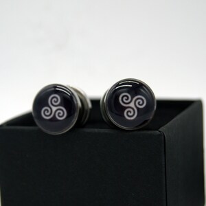 May include: A pair of silver cufflinks with a black background and a white Celtic knot design.