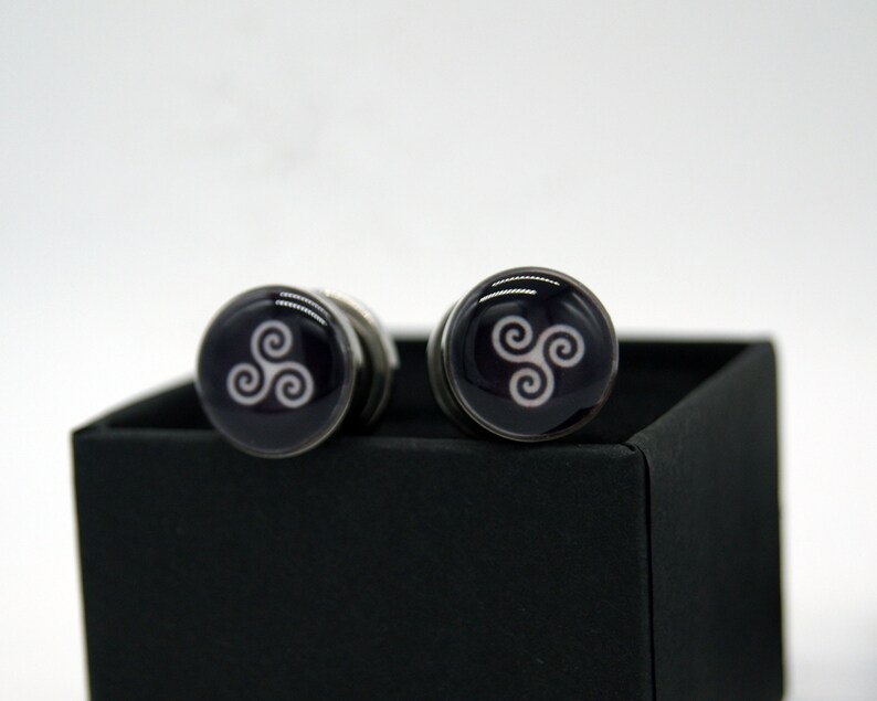 May include: A pair of silver cufflinks with a black background and a white Celtic knot design.