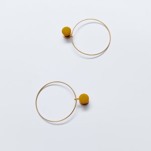 May include: A pair of gold hoop earrings with a mustard yellow circle pendant on each hoop.