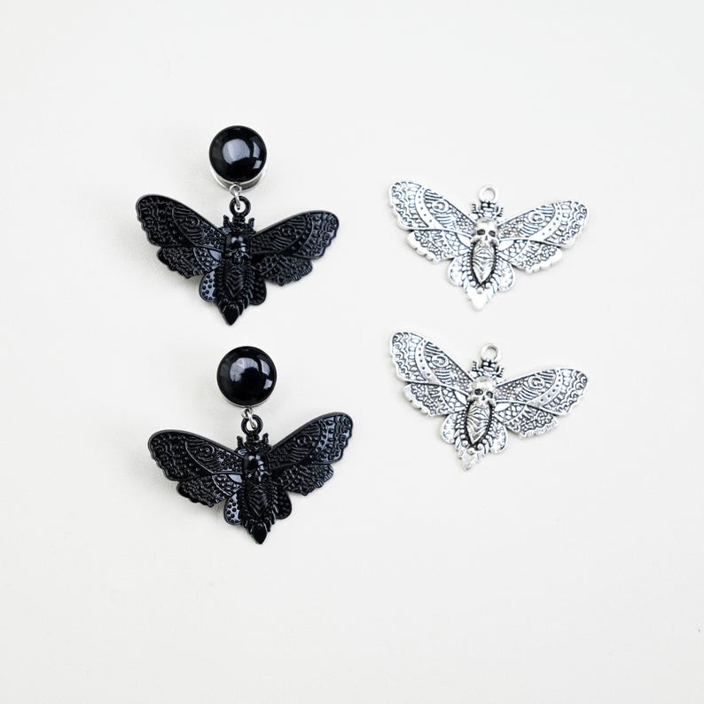 May include: Black and silver-toned moth-shaped earrings and charms. Two pairs of black earrings feature a black ball stud and a moth pendant. Two silver-toned moth charms are also displayed, showcasing intricate wing details.