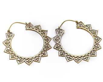 May include: A pair of gold-colored hoop earrings. Each earring features a circular design with an intricate, openwork pattern. The outer edge has heart-shaped cutouts, and the overall style is ornate and decorative.