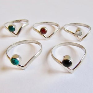 May include: Five silver rings with different coloured gemstones. The rings are all V-shaped and have a simple design.
