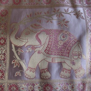 May include: A pink and gold embroidered fabric with an elephant design. The elephant is outlined in gold thread and has pink and gold details. The fabric has a floral border.