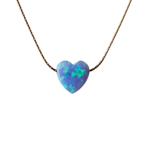 Puede incluir: Un delicado collar de cadena dorada con un colgante de &oacute;palo en forma de coraz&oacute;n. El &oacute;palo es de un azul vibrante con destellos verdes y morados.