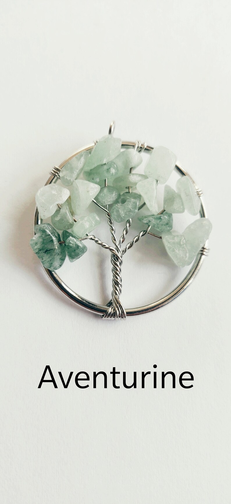 Puede incluir: Un colgante de &aacute;rbol de la vida envuelto en alambre plateado con piedras de aventurina verde.