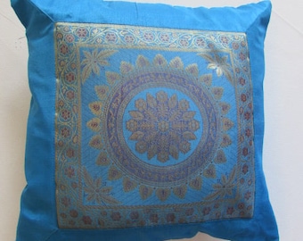 May include: A blue throw pillow with a gold and silver patterned design. The pattern features a large, intricate floral motif in the center.