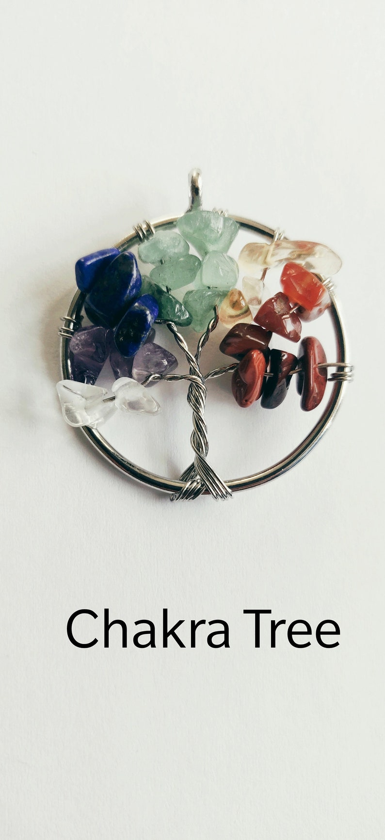 Puede incluir: Un colgante de &aacute;rbol de la vida envuelto en alambre plateado con siete piedras de chakra. Las piedras son transparentes, amatista, azules, verdes, amarillas, naranjas y rojas.