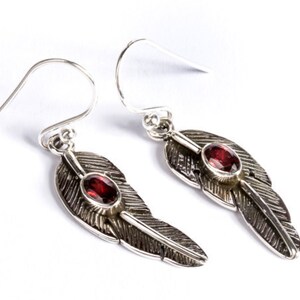 May include: Silver dangle earrings with a feather design and a red gemstone accent.